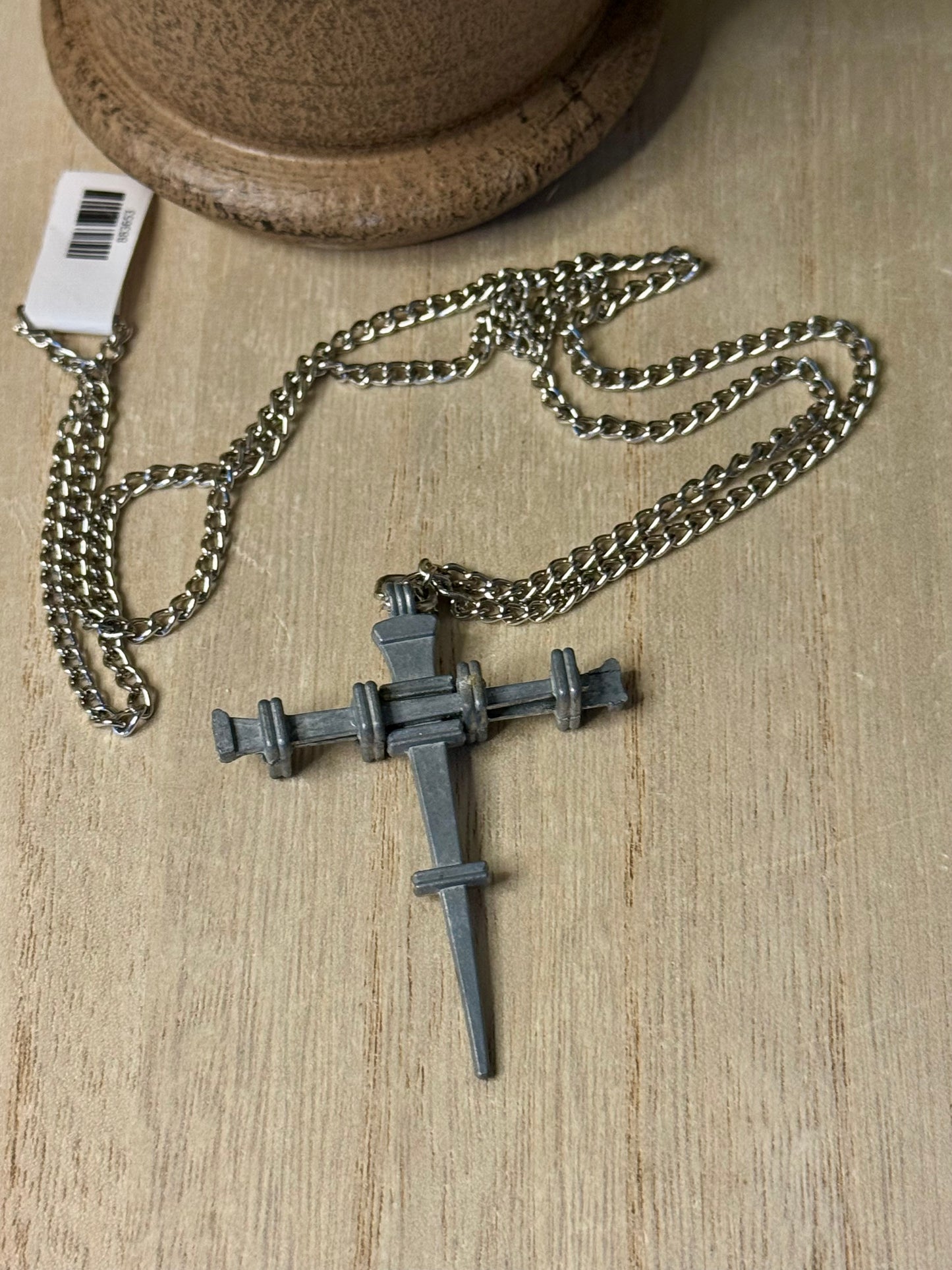 Metallic cross pendant on a chain with a tag on a wooden surface