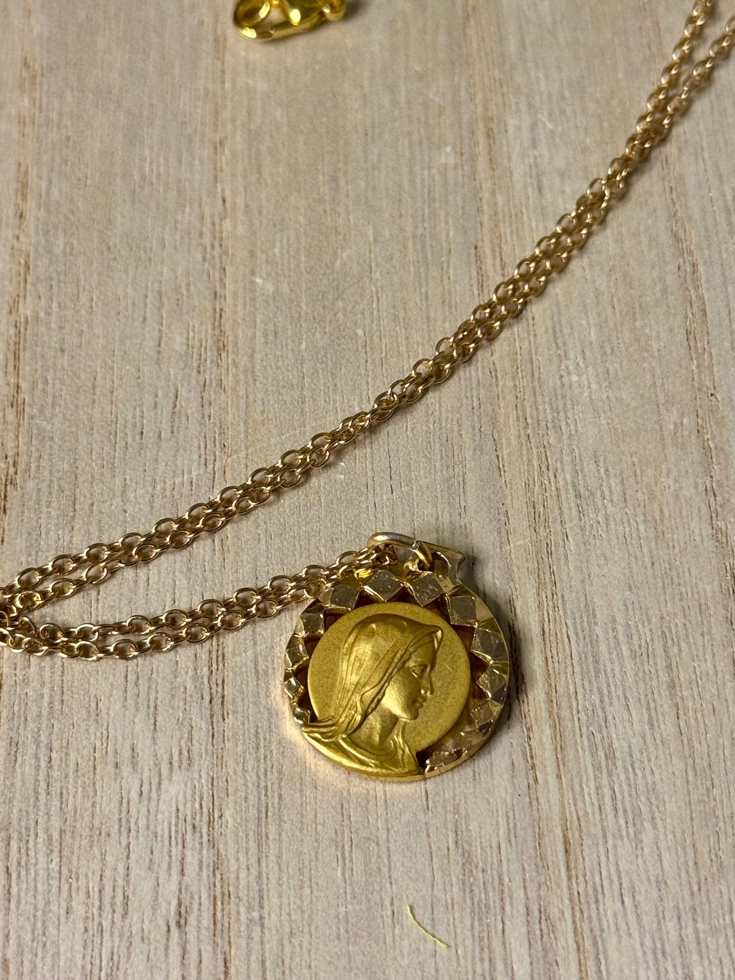 Gold necklace with a round pendant on a light wooden surface