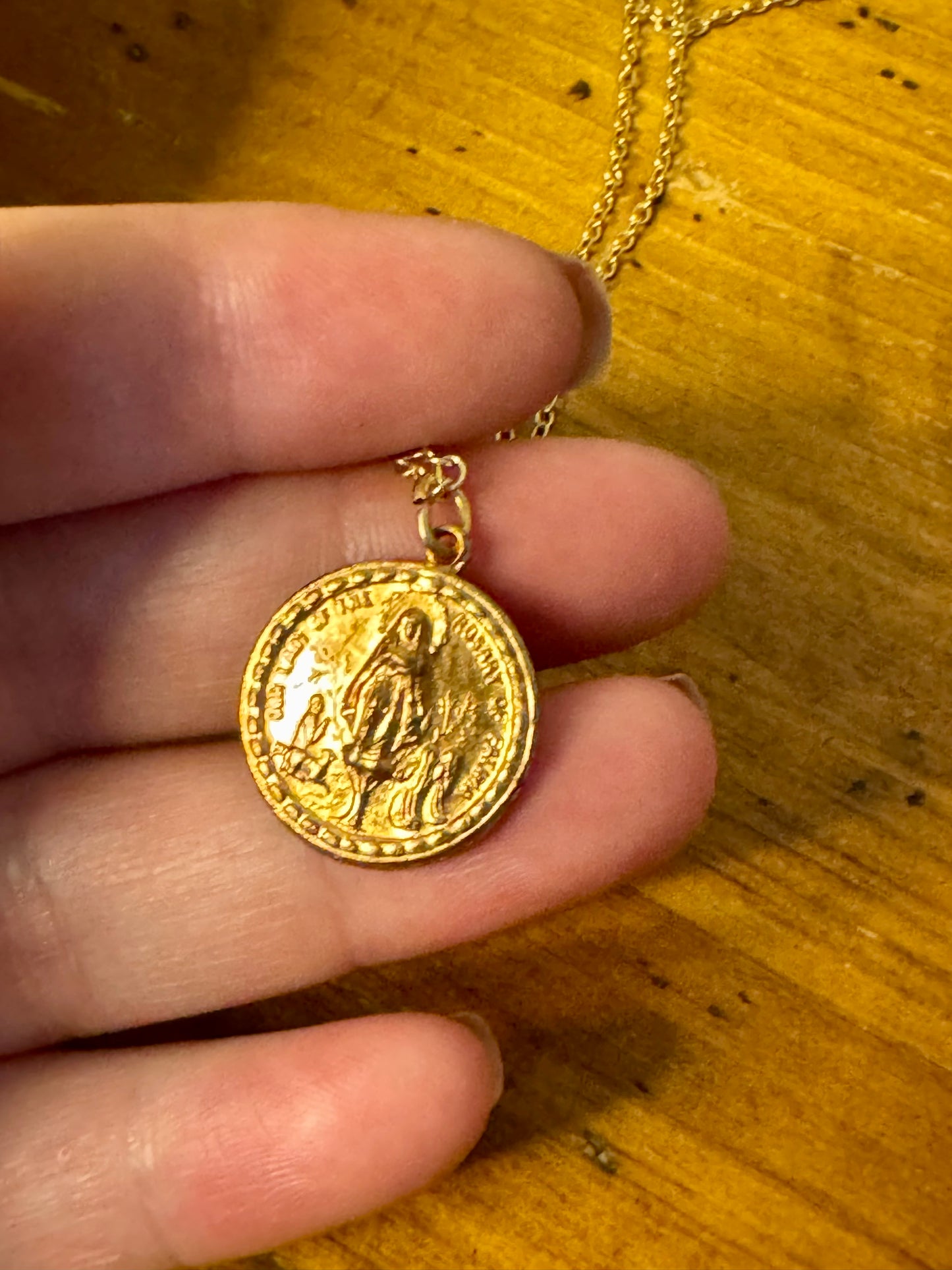 Gold coin pendant held by a hand on a wooden surface