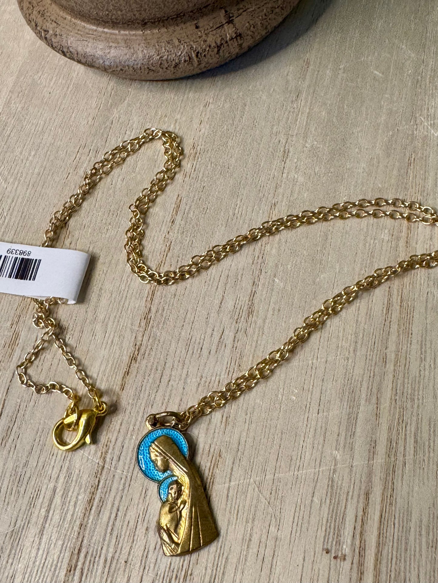 Gold necklace with a pendant featuring a religious figure on a wooden surface