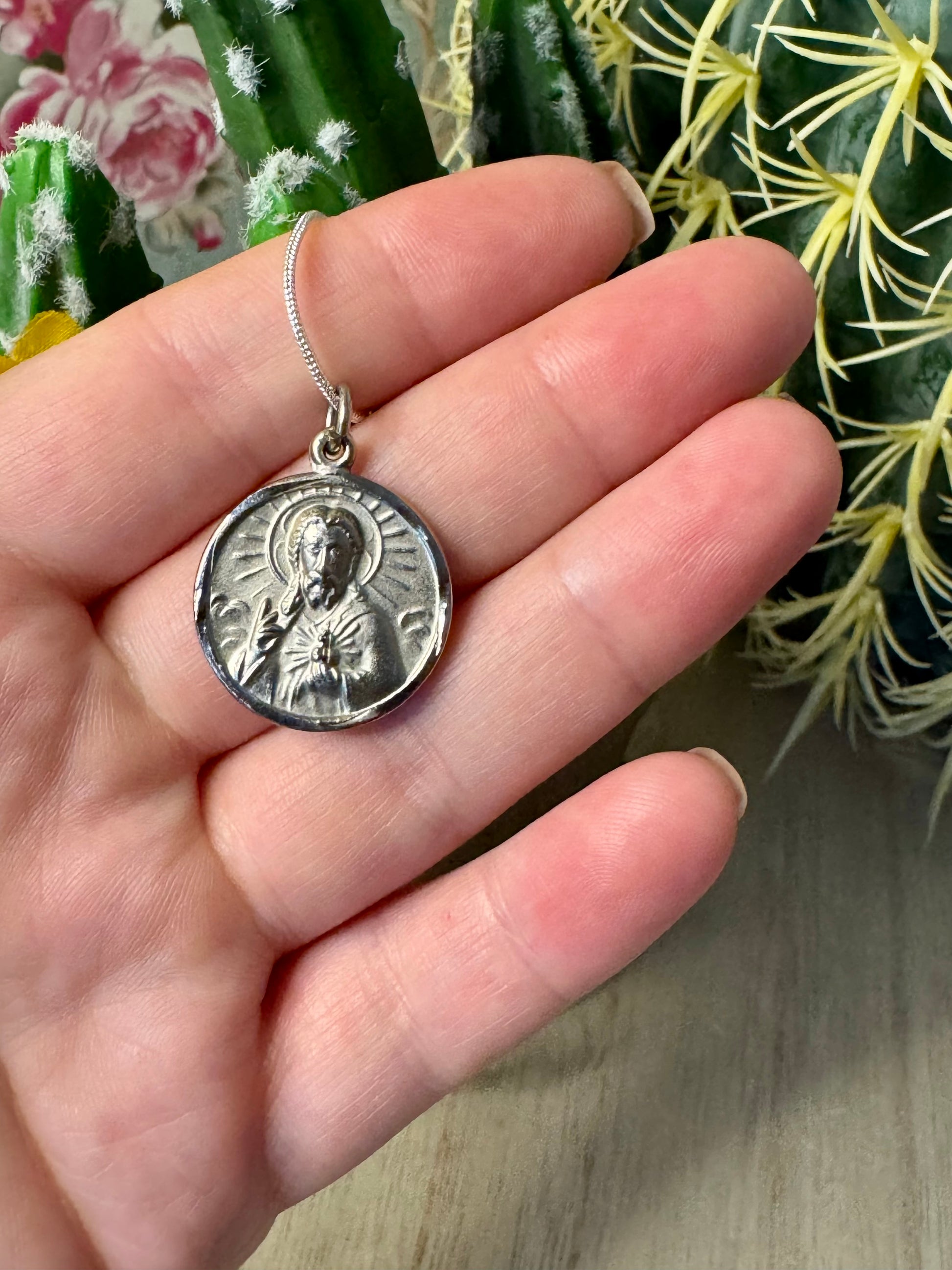 Silver pendant held in a hand with cacti in the background