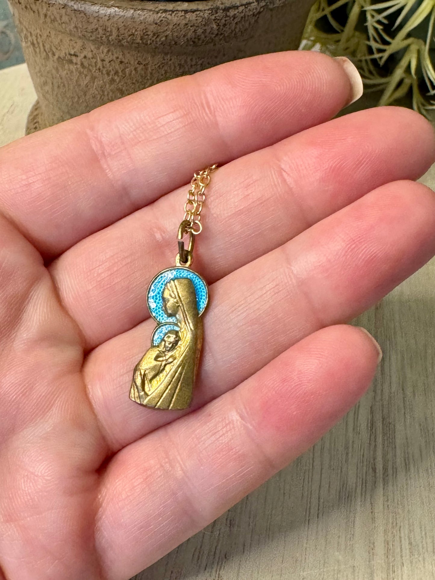 Gold necklace with a pendant of a religious figure held in a hand.