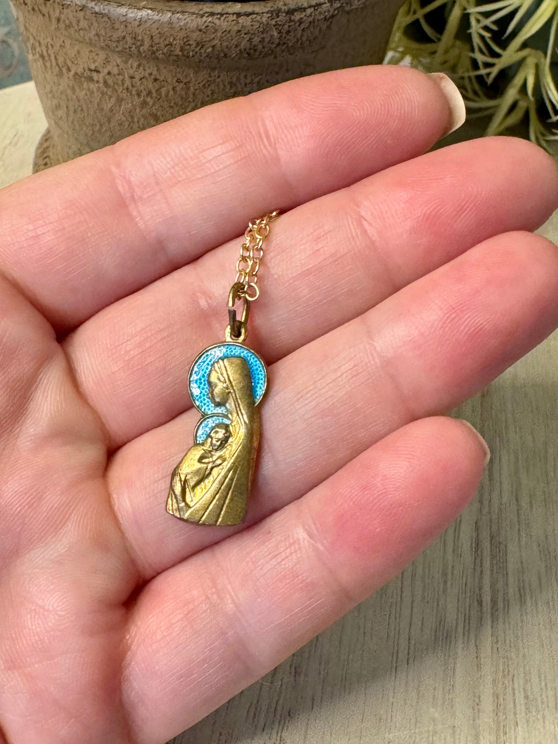 Gold necklace with a pendant of a religious figure held in a hand.