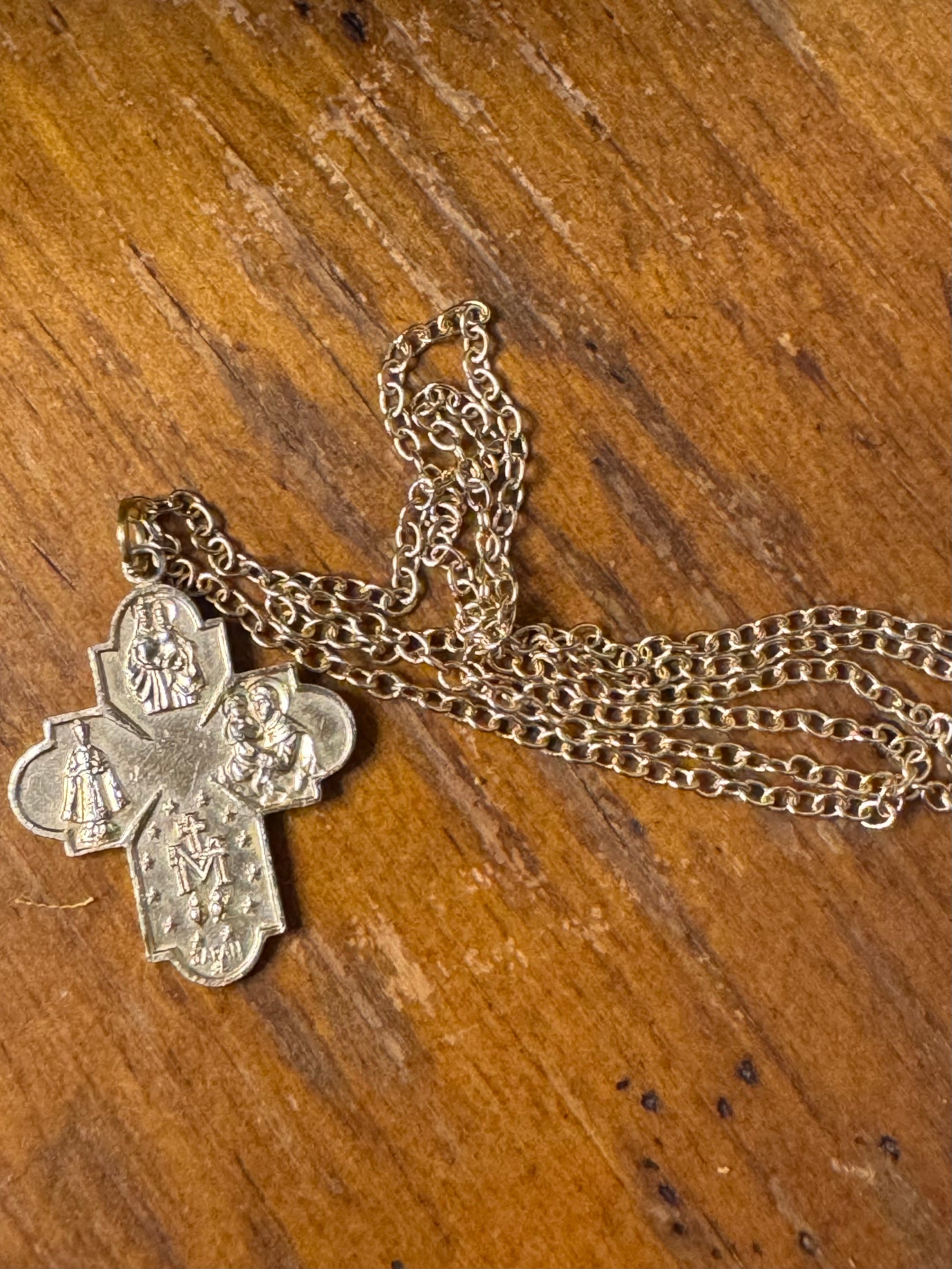 Silver cross pendant on a chain against a wooden background