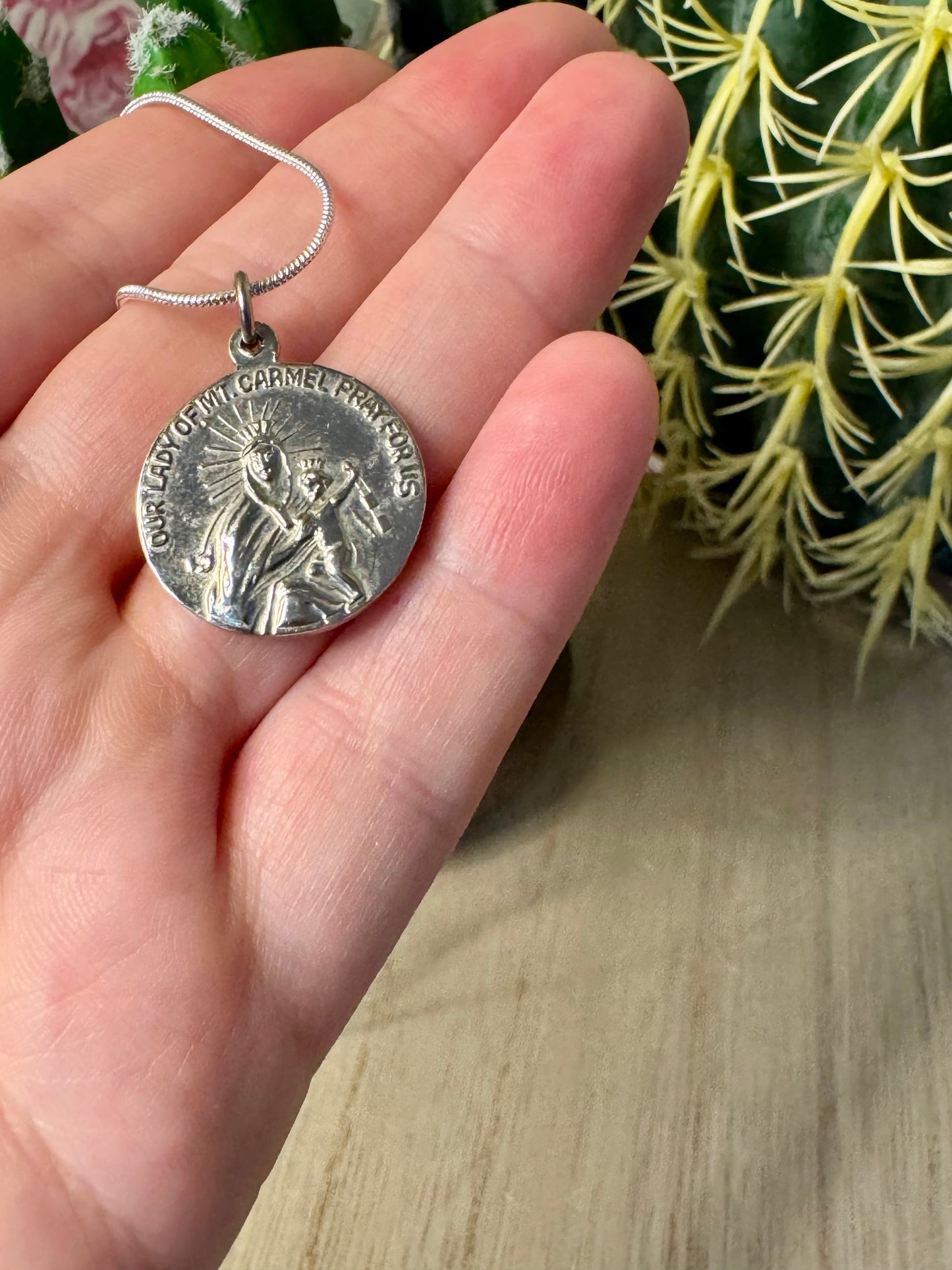 Silver religious pendant on a chain held in a hand with a blurred background
