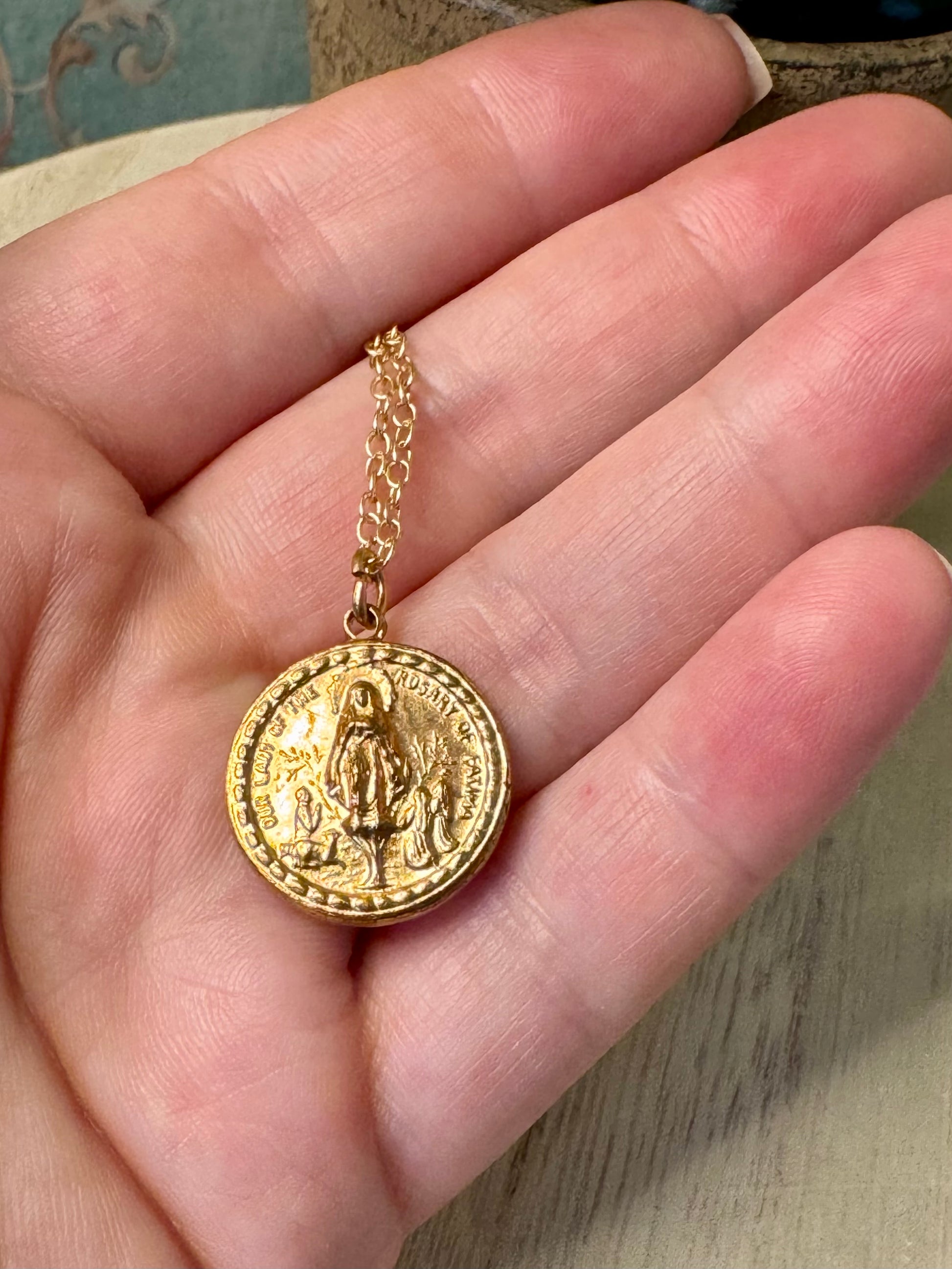 Gold necklace with a round pendant held in a hand against a neutral background