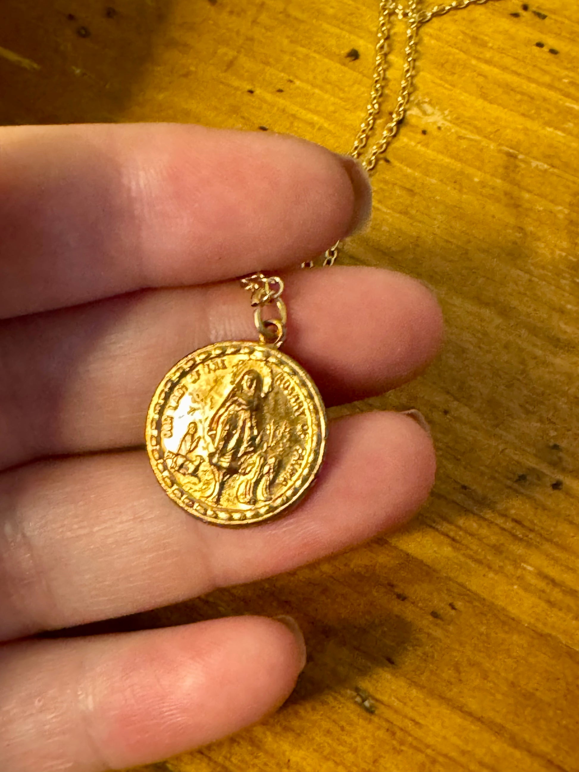 Gold coin pendant held by a hand on a wooden surface