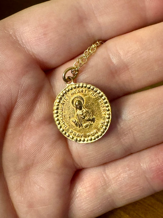 Gold necklace with a religious pendant held in a hand.