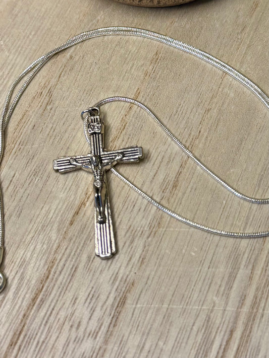 Silver cross pendant on a chain against a wooden background