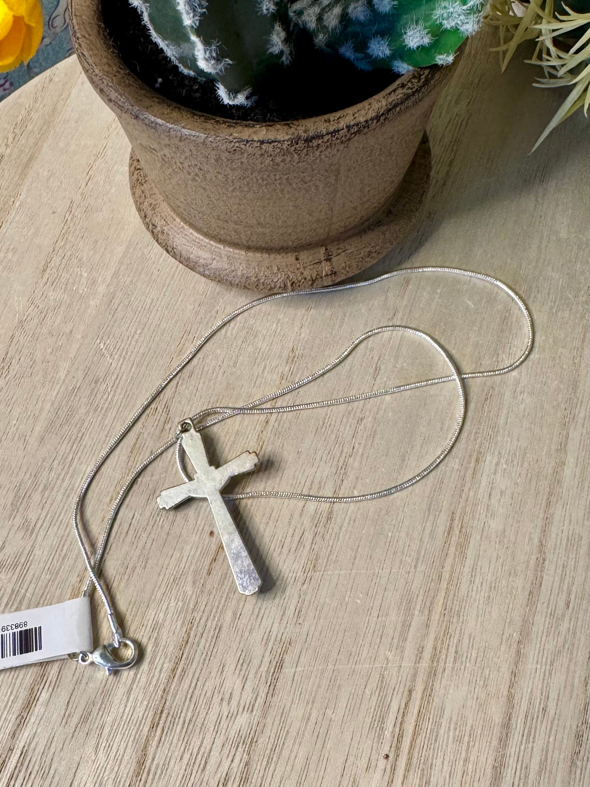 Silver cross necklace on a wooden surface with a plant in the background
