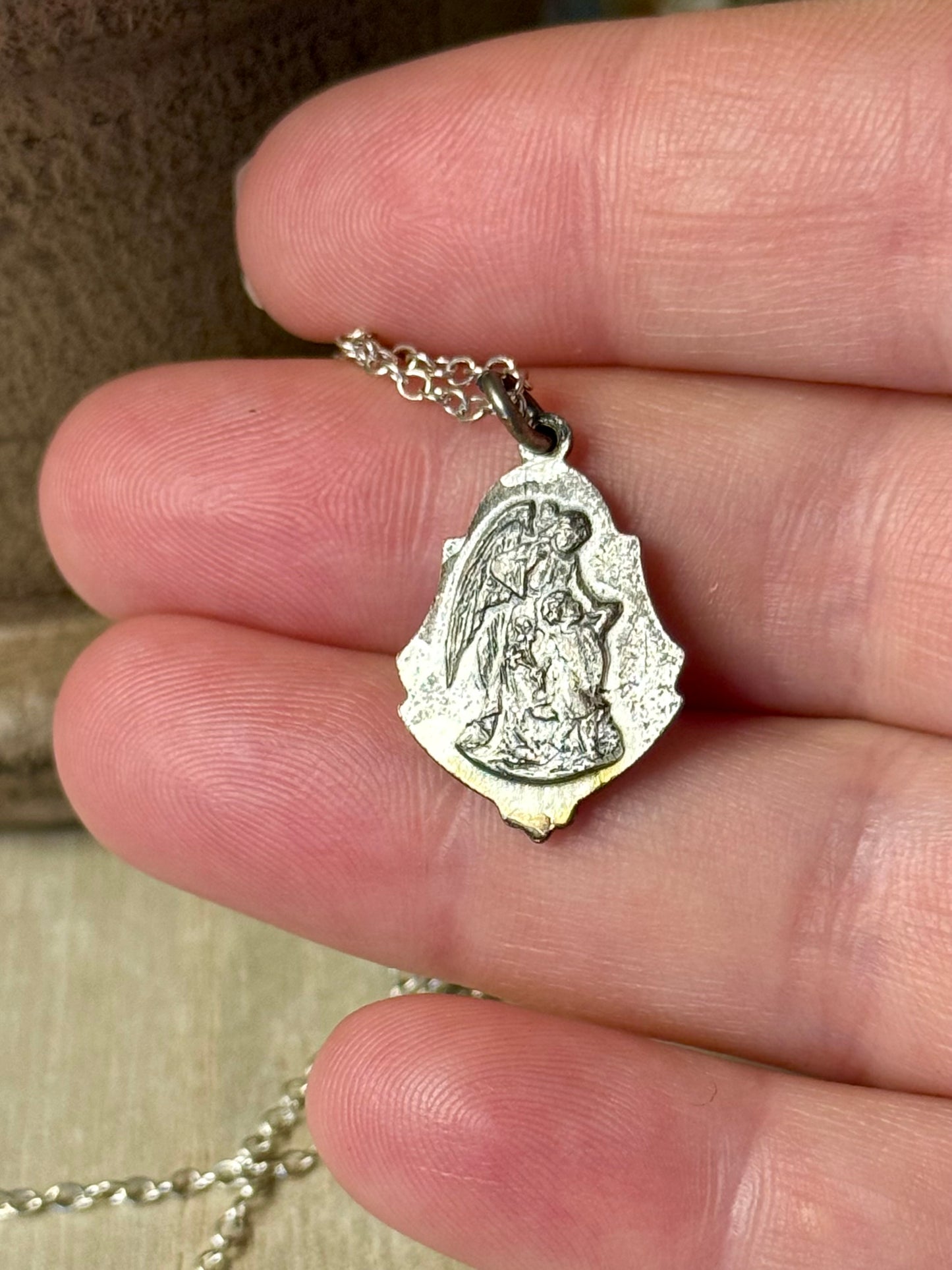 Silver angel pendant necklace held between fingers