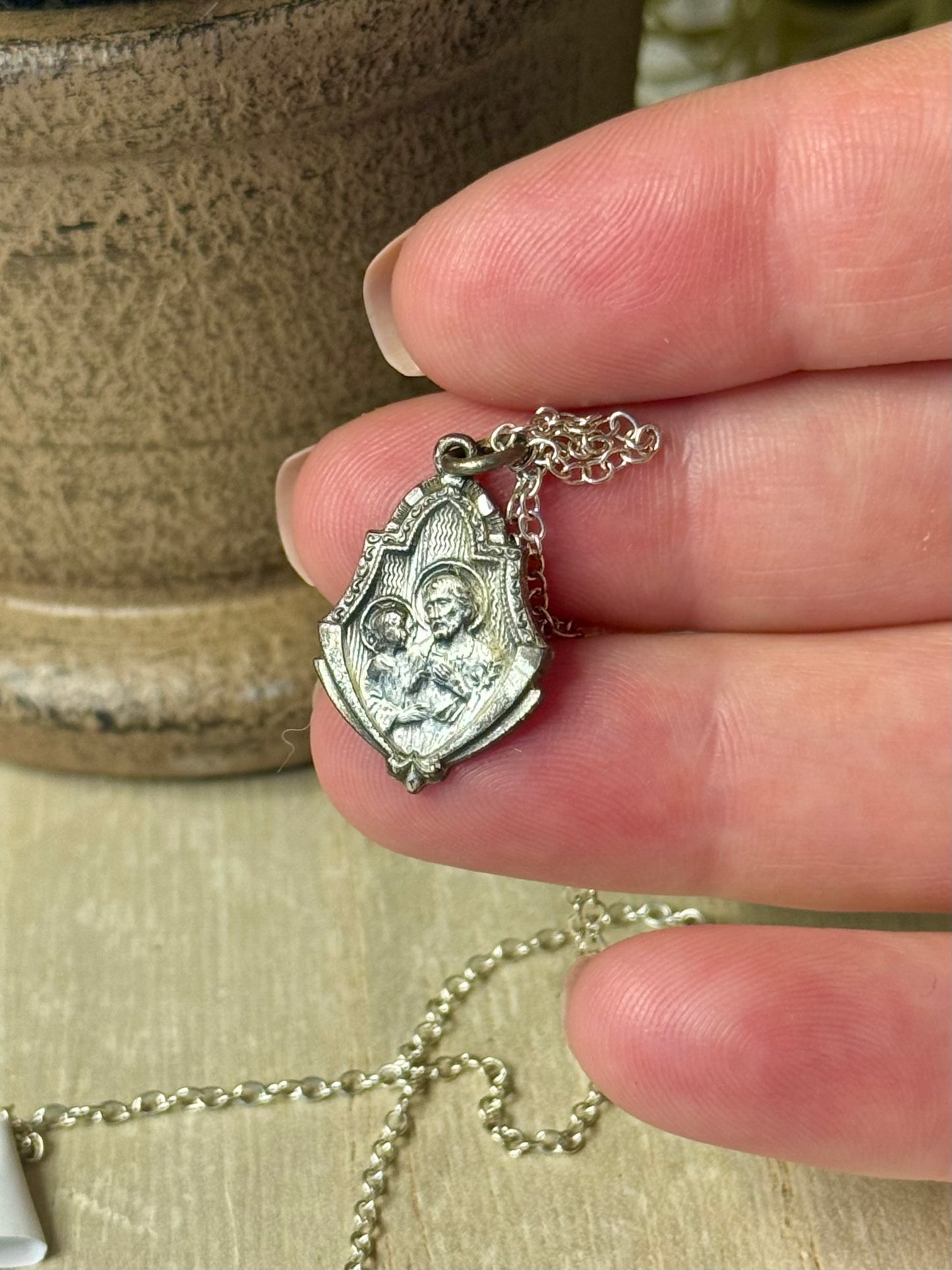 Silver pendant with a religious design held in a hand against a neutral background