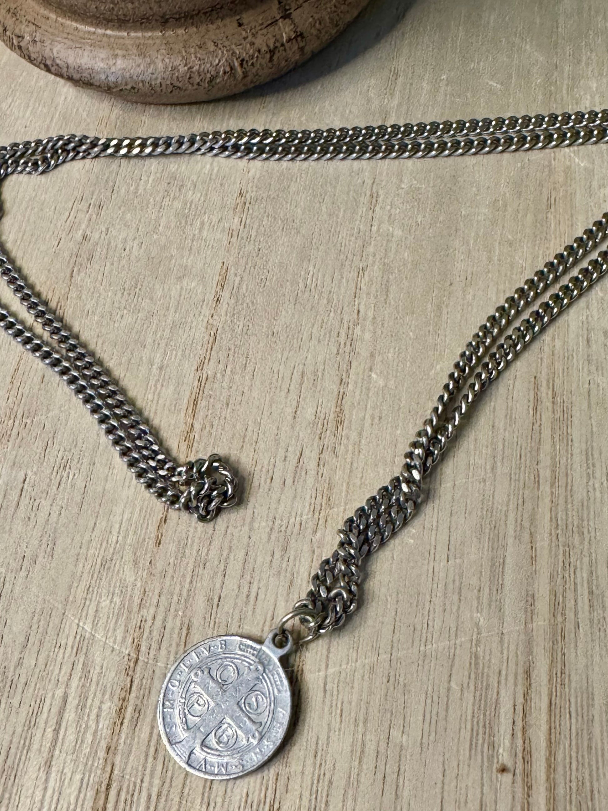 Silver chain necklace with a round pendant on a wooden surface