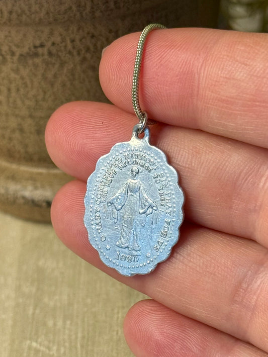 Silver religious pendant held between fingers with a blurred background